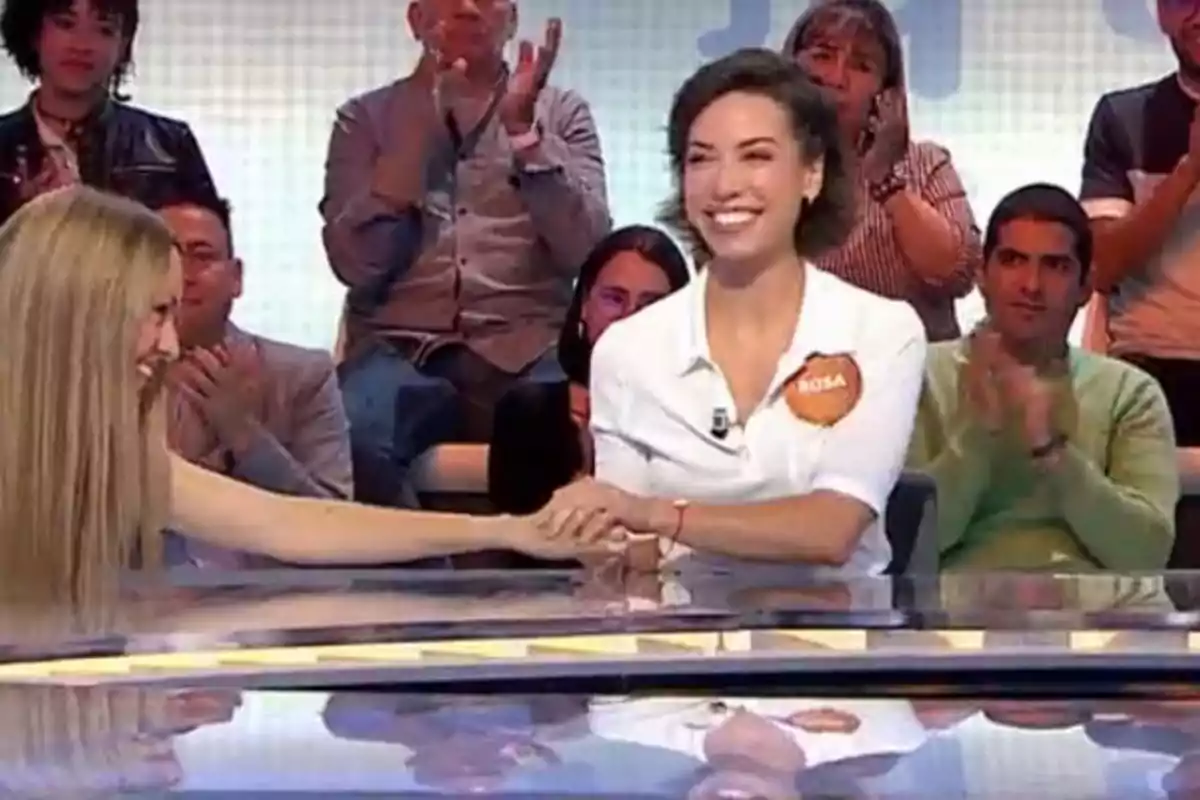 Rosa y Esmeralda Moya sonríen y se toman de las manos en un programa de concursos mientras el público aplaude en el fondo Rosa y Esmeralda Moya sonríen y se toman de las manos en un programa de concursos mientras el público aplaude en el fondo