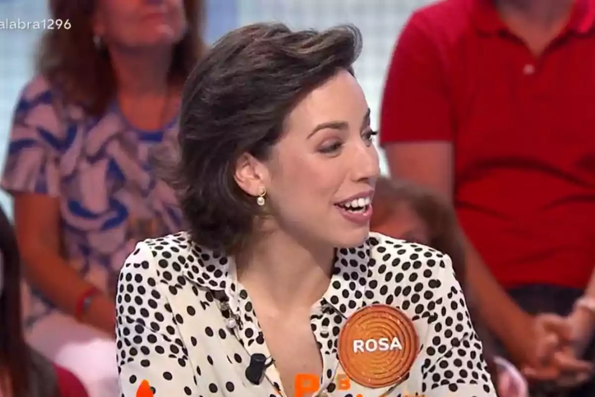 Rosa de cabello corto y oscuro con blusa de lunares blancos y negros participando en un programa de televisión con una placa que dice Rosa Rosa de cabello corto y oscuro con blusa de lunares blancos y negros participando en un programa de televisión con una placa que dice Rosa