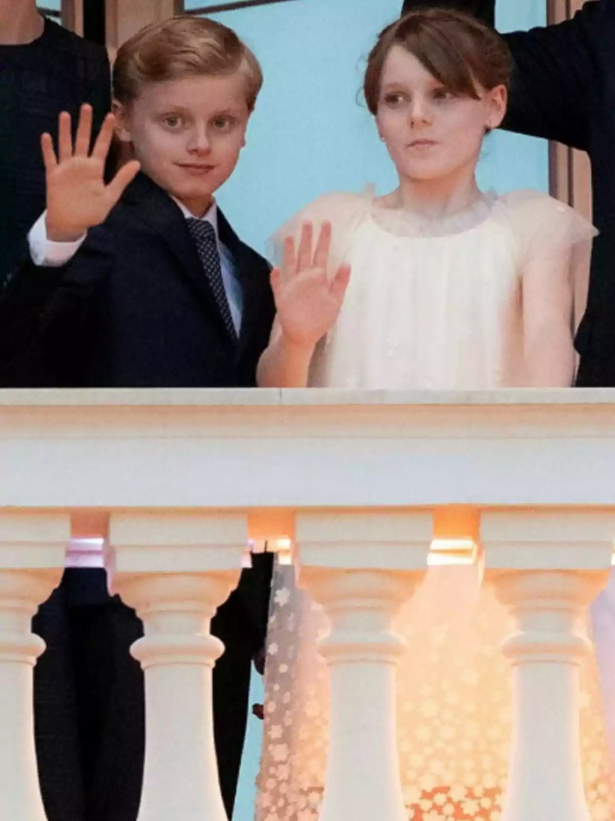Dos niños elegantemente vestidos saludan desde un balcón Dos niños elegantemente vestidos saludan desde un balcón