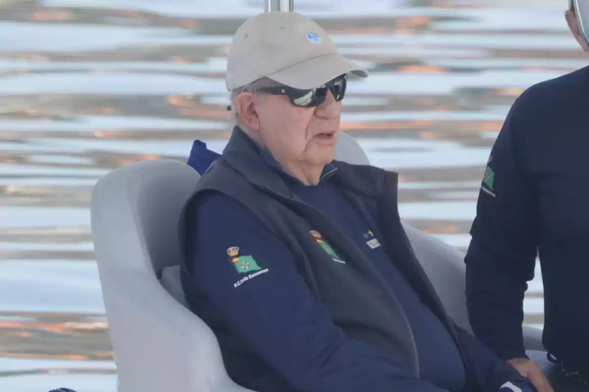 Juan Carlos I wearing a cap and sunglasses sitting in a boat on the water Juan Carlos I wearing a cap and sunglasses sitting in a boat on the water