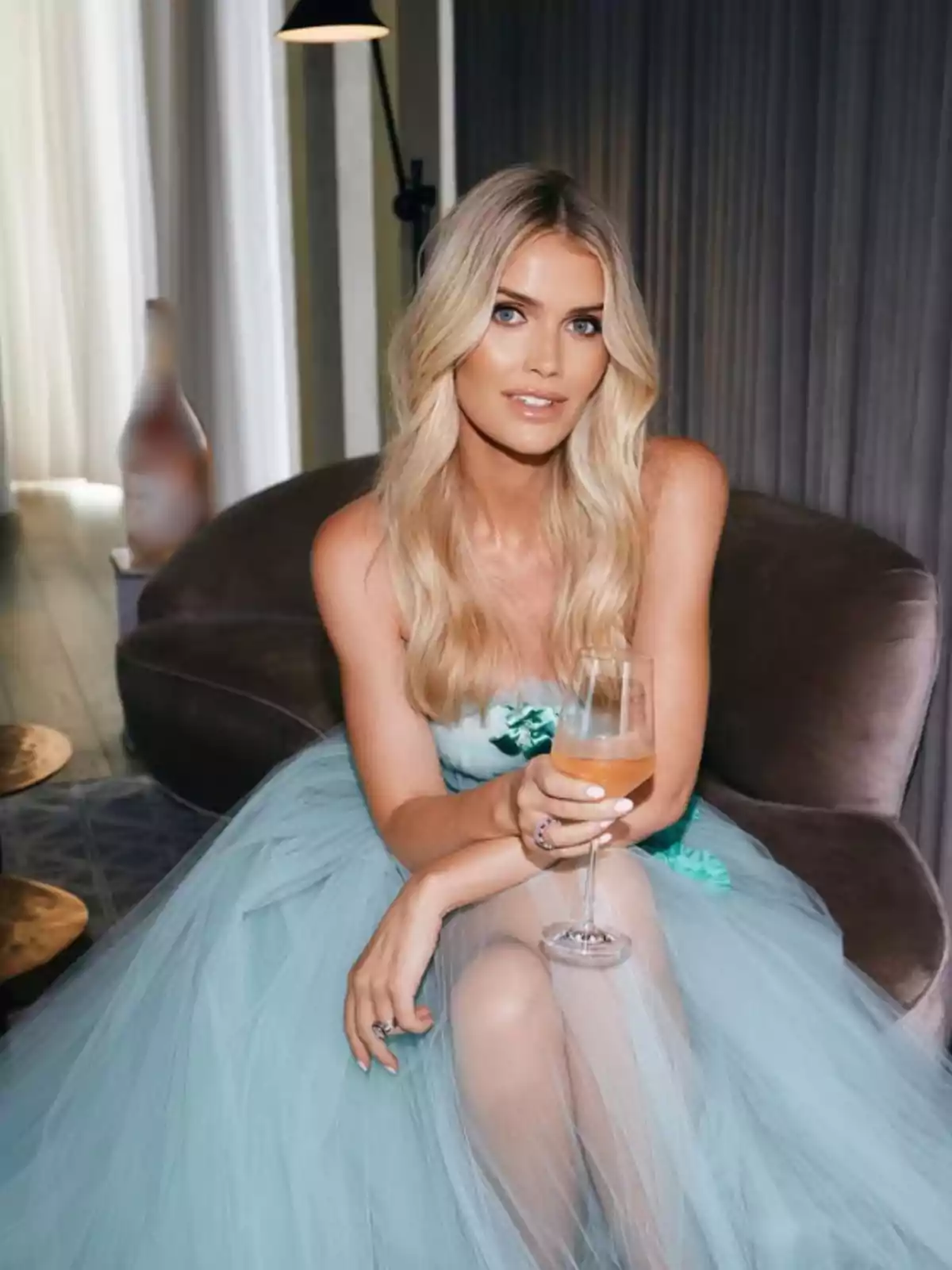 Mujer rubia con vestido azul claro sentada en un sillón sosteniendo una copa de vino rosado Mujer rubia con vestido azul claro sentada en un sillón sosteniendo una copa de vino rosado