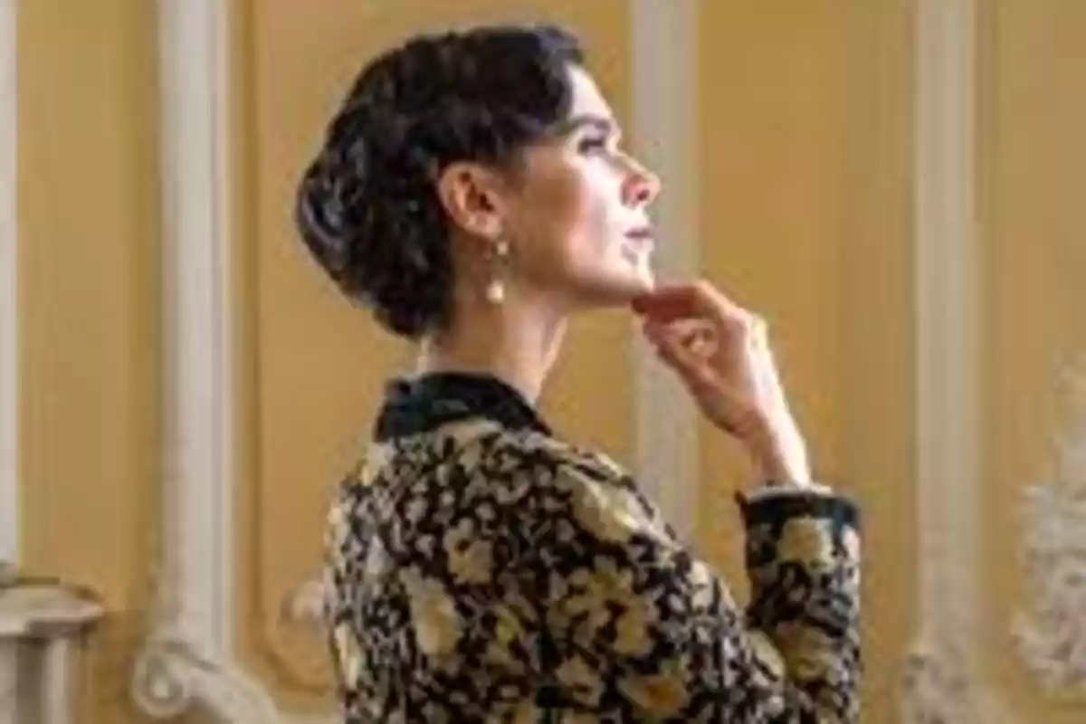 Esmeralda elegante de perfil con el cabello recogido y un abrigo de flores doradas en un ambiente clásico. Captura de 'La Promesa' Esmeralda elegante de perfil con el cabello recogido y un abrigo de flores doradas en un ambiente clásico. Captura de 'La Promesa'