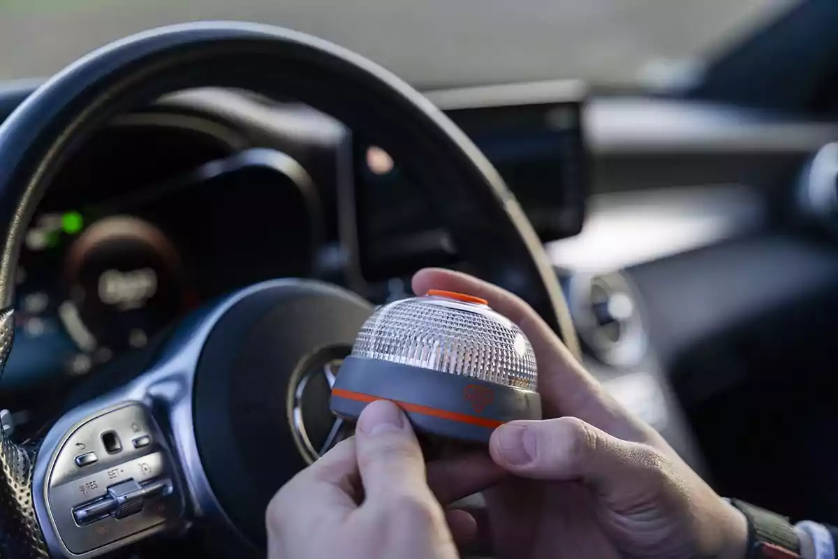Persona dentro de un automóvil sosteniendo una luz de emergencia portátil frente al volante