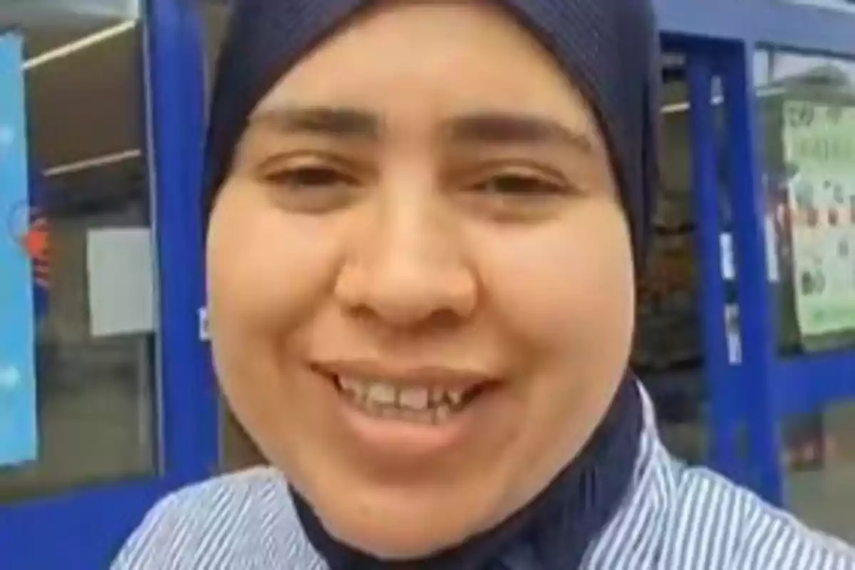 Mujer sonriendo con un pañuelo en la cabeza frente a la entrada de una tienda Mujer sonriendo con un pañuelo en la cabeza frente a la entrada de una tienda