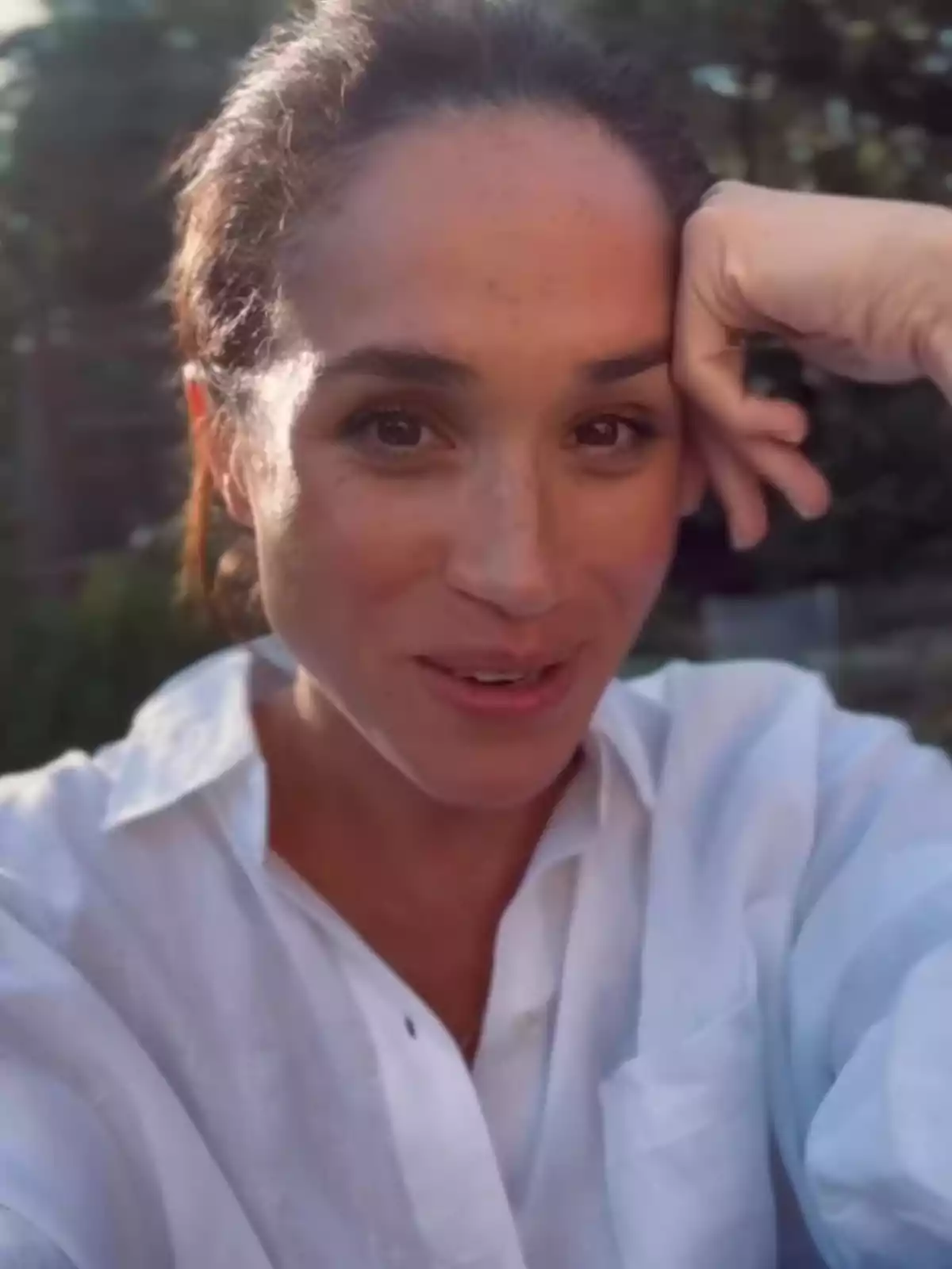 Woman in a white jersey smiling and resting her head on her hand in an outdoor setting Woman in a white jersey smiling and resting her head on her hand in an outdoor setting