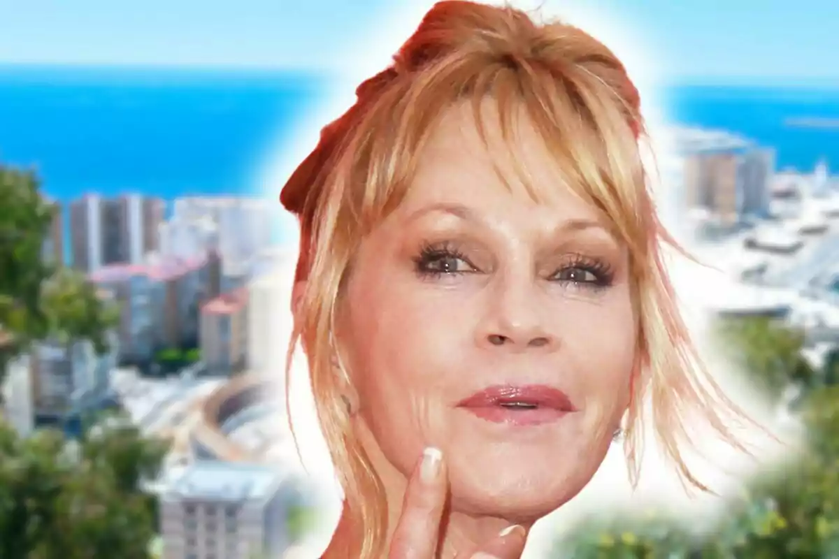 Melanie Griffith con expresión pensativa en primer plano con una ciudad costera de Málaga y el mar de fondo desenfocados.