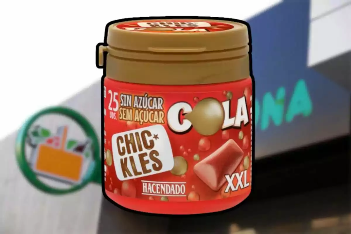 Envase de chicles sabor cola sin azúcar de la marca Hacendado en tamaño XXL frente a una tienda Mercadona desenfocada. Envase de chicles sabor cola sin azúcar de la marca Hacendado en tamaño XXL frente a una tienda Mercadona desenfocada.