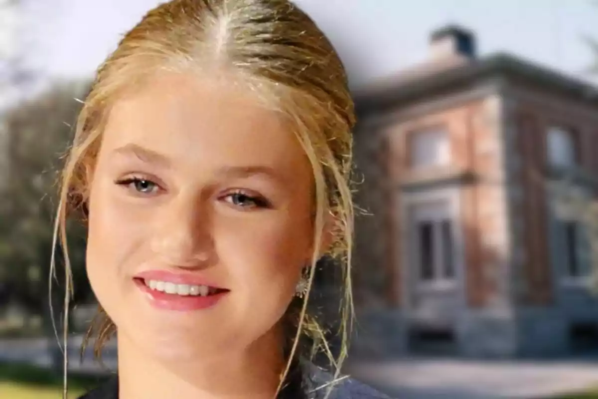 Primer plano de la princesa Leonor sonriente con el cabello recogido frente a un edificio de ladrillo desenfocado, el cual es el palacio de la Zarzuela.