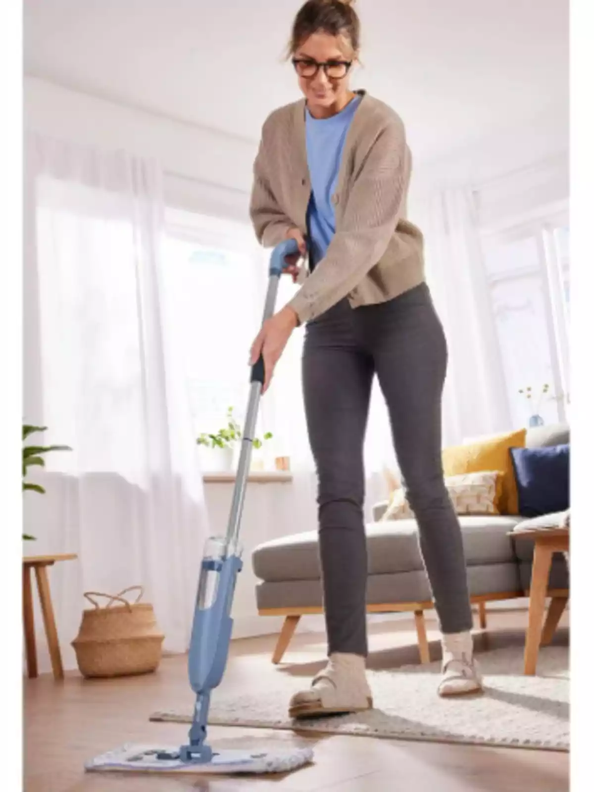 Mujer joven limpiando el suelo de una sala moderna y luminosa con un trapeador azul Mujer joven limpiando el suelo de una sala moderna y luminosa con un trapeador azul