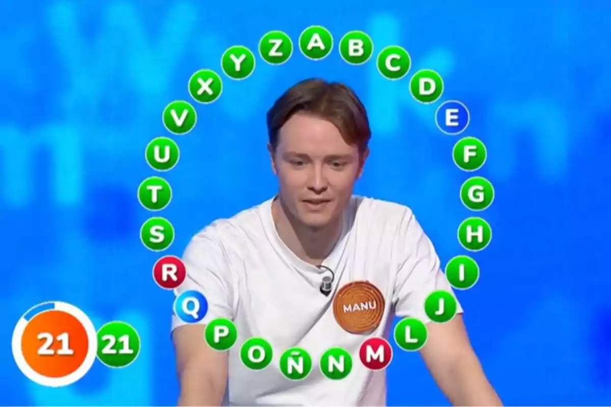Manu participa en la prueba final del rosco en un programa de televisión de preguntas y respuestas con letras en círculo y un marcador de tiempo mostrando 21 segundos. Captura de 'Pasapalabra' Manu participa en la prueba final del rosco en un programa de televisión de preguntas y respuestas con letras en círculo y un marcador de tiempo mostrando 21 segundos. Captura de 'Pasapalabra'