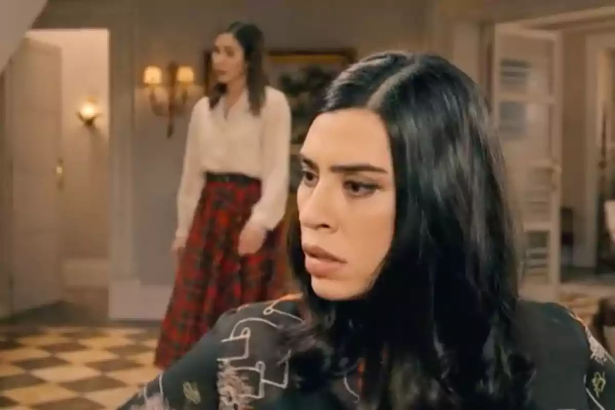 María en primer plano con expresión seria mientras Begoña de fondo camina en una habitación elegante. Captura de 'Sueños de libertad' María en primer plano con expresión seria mientras Begoña de fondo camina en una habitación elegante. Captura de 'Sueños de libertad'