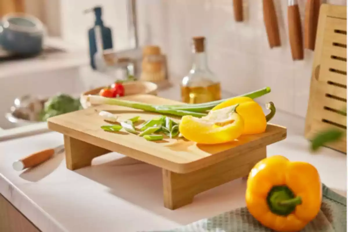 Pimientos amarillos y cebollines frescos sobre una tabla de cortar en una cocina iluminada Pimientos amarillos y cebollines frescos sobre una tabla de cortar en una cocina iluminada