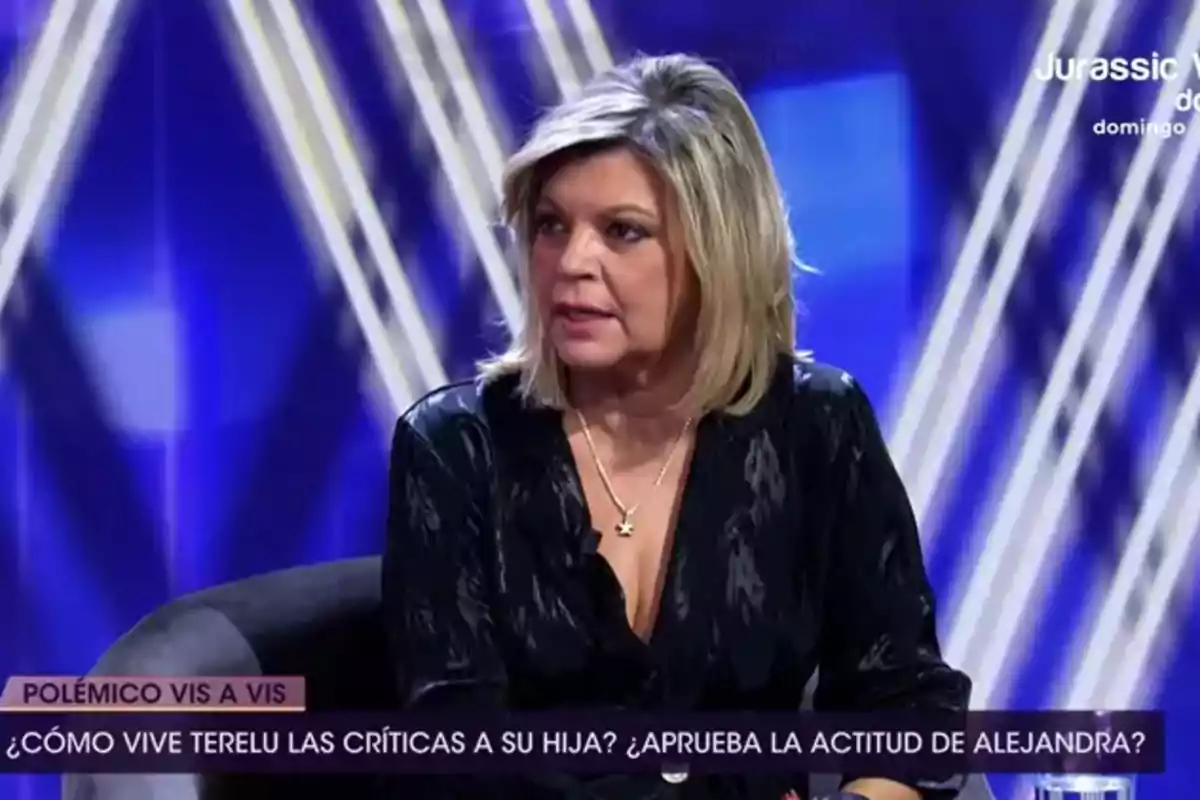 Terelu Campos con cabello corto sentada en un plató de televisión con fondo azul y luces, participando en una entrevista o debate Terelu Campos con cabello corto sentada en un plató de televisión con fondo azul y luces, participando en una entrevista o debate