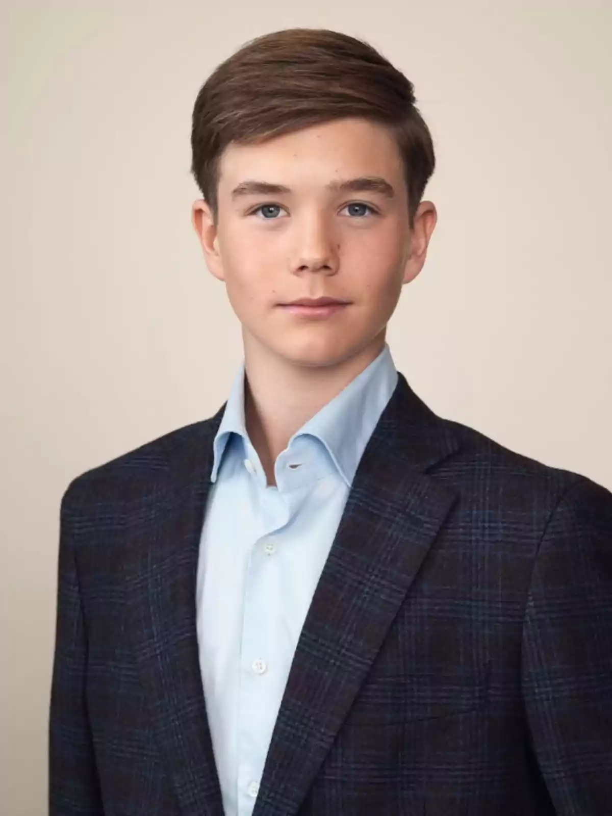 Young man with short brown hair wearing a dark checkered blazer and light blue jersey posing in front of a beige background Young man with short brown hair wearing a dark checkered blazer and light blue jersey posing in front of a beige background