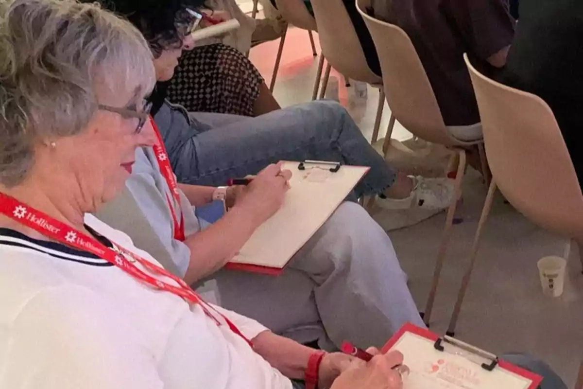 Personas sentadas en sillas tomando notas en hojas sujetas con portapapeles durante un evento o conferencia