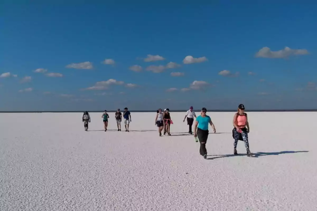 Grupo de personas caminando sobre un extenso salar bajo un cielo azul con algunas nubes dispersas Grupo de personas caminando sobre un extenso salar bajo un cielo azul con algunas nubes dispersas
