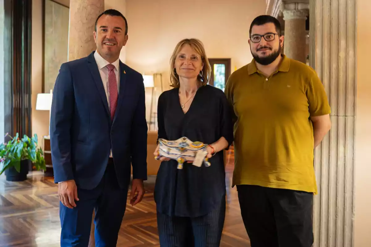 Tres personas posan juntas en un interior elegante, la mujer en el centro sostiene un objeto decorativo de cerámica y todos miran a la cámara sonriendo. Tres personas posan juntas en un interior elegante, la mujer en el centro sostiene un objeto decorativo de cerámica y todos miran a la cámara sonriendo.