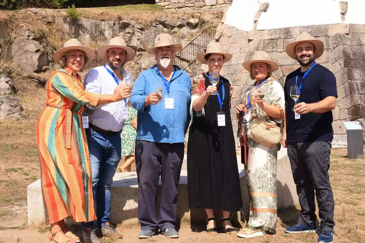 Grupo de seis personas sonrientes con sombreros y copas de vino en la mano posando al aire libre frente a una construcción de piedra