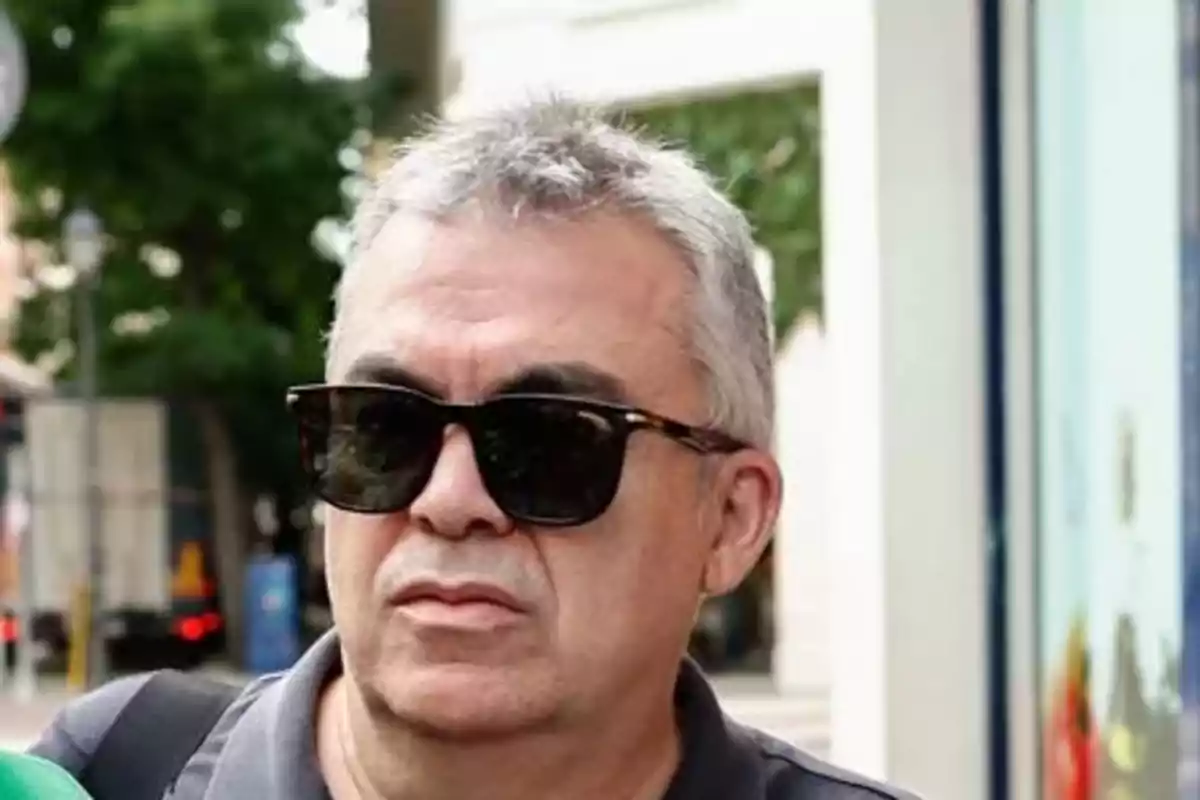 Hombre de cabello canoso y corto usando gafas de sol oscuras y camiseta gris en una calle urbana Hombre de cabello canoso y corto usando gafas de sol oscuras y camiseta gris en una calle urbana