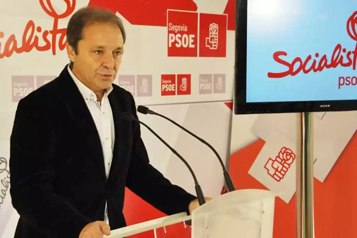 Hombre hablando en un atril durante una rueda de prensa del PSOE en Segovia con logotipos y carteles del partido al fondo Hombre hablando en un atril durante una rueda de prensa del PSOE en Segovia con logotipos y carteles del partido al fondo