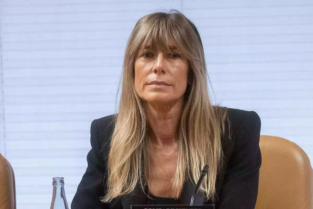 Mujer de cabello rubio largo y lacio con flequillo sentada en una mesa de conferencia con fondo de persianas blancas Mujer de cabello rubio largo y lacio con flequillo sentada en una mesa de conferencia con fondo de persianas blancas