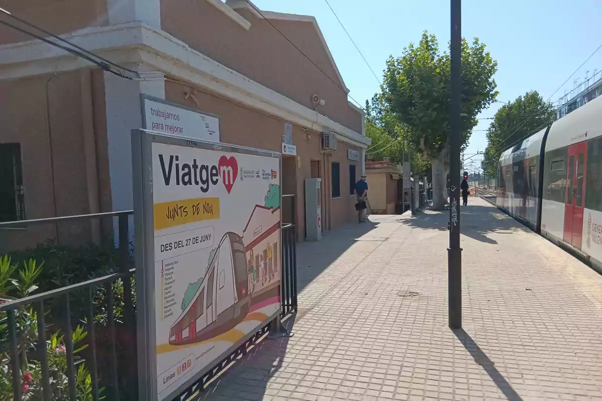 Estación de tren con un cartel publicitario de la Generalitat Valenciana que anuncia el regreso del servicio, un tren detenido y personas caminando por el andén en un día soleado. Estación de tren con un cartel publicitario de la Generalitat Valenciana que anuncia el regreso del servicio, un tren detenido y personas caminando por el andén en un día soleado.