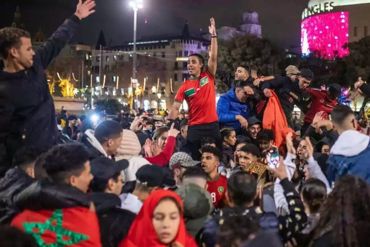 Multitud de personas celebrando en la calle durante la noche, muchas de ellas llevan camisetas y banderas de Marruecos, algunas personas están subidas sobre los hombros de otras y se ven luces y edificios al fondo Multitud de personas celebrando en la calle durante la noche, muchas de ellas llevan camisetas y banderas de Marruecos, algunas personas están subidas sobre los hombros de otras y se ven luces y edificios al fondo