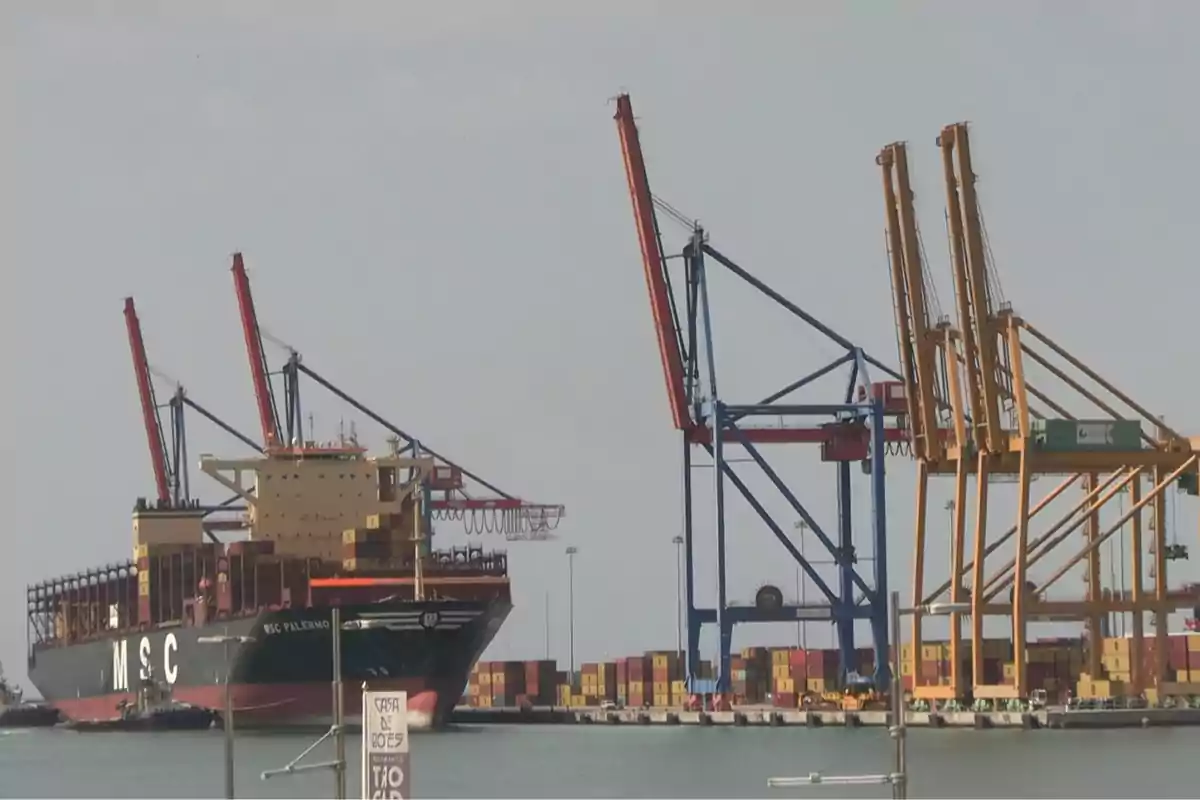 Un barco portacontenedores atracado en un puerto con varias grúas y contenedores apilados Un barco portacontenedores atracado en un puerto con varias grúas y contenedores apilados