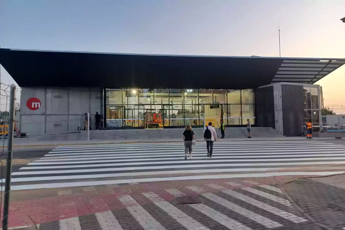 Personas cruzan un paso de cebra hacia la entrada de una estación de metro moderna al atardecer