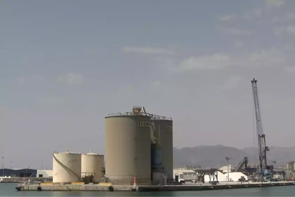 Silos industriales junto al mar con una grúa y montañas al fondo en un día despejado Silos industriales junto al mar con una grúa y montañas al fondo en un día despejado