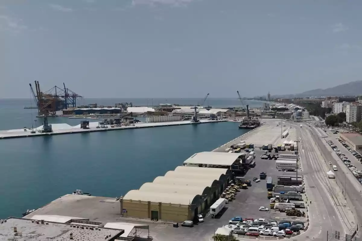 Vista panorámica de un puerto industrial con grúas, almacenes, contenedores y vehículos junto al mar en un día despejado Vista panorámica de un puerto industrial con grúas, almacenes, contenedores y vehículos junto al mar en un día despejado