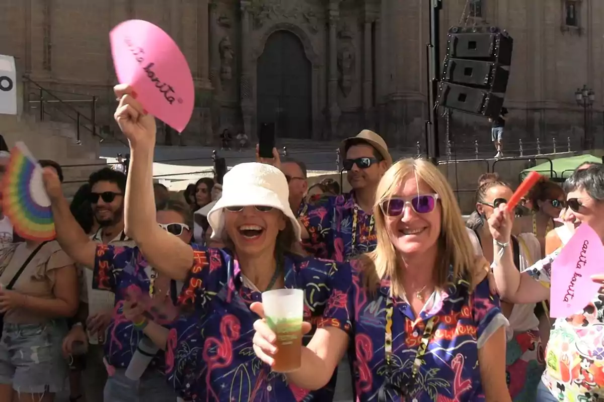 Grupo de personas sonrientes con camisas coloridas y abanicos disfrutando de una fiesta al aire libre frente a un edificio histórico Grupo de personas sonrientes con camisas coloridas y abanicos disfrutando de una fiesta al aire libre frente a un edificio histórico