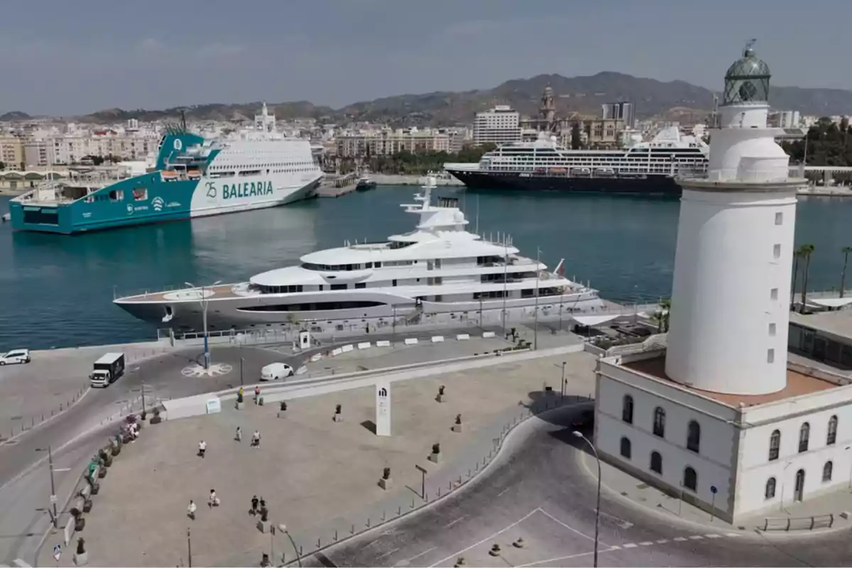 Vista del puerto con un faro blanco en primer plano, un gran yate atracado y dos barcos de pasajeros al fondo, con la ciudad y montañas en el horizonte Vista del puerto con un faro blanco en primer plano, un gran yate atracado y dos barcos de pasajeros al fondo, con la ciudad y montañas en el horizonte