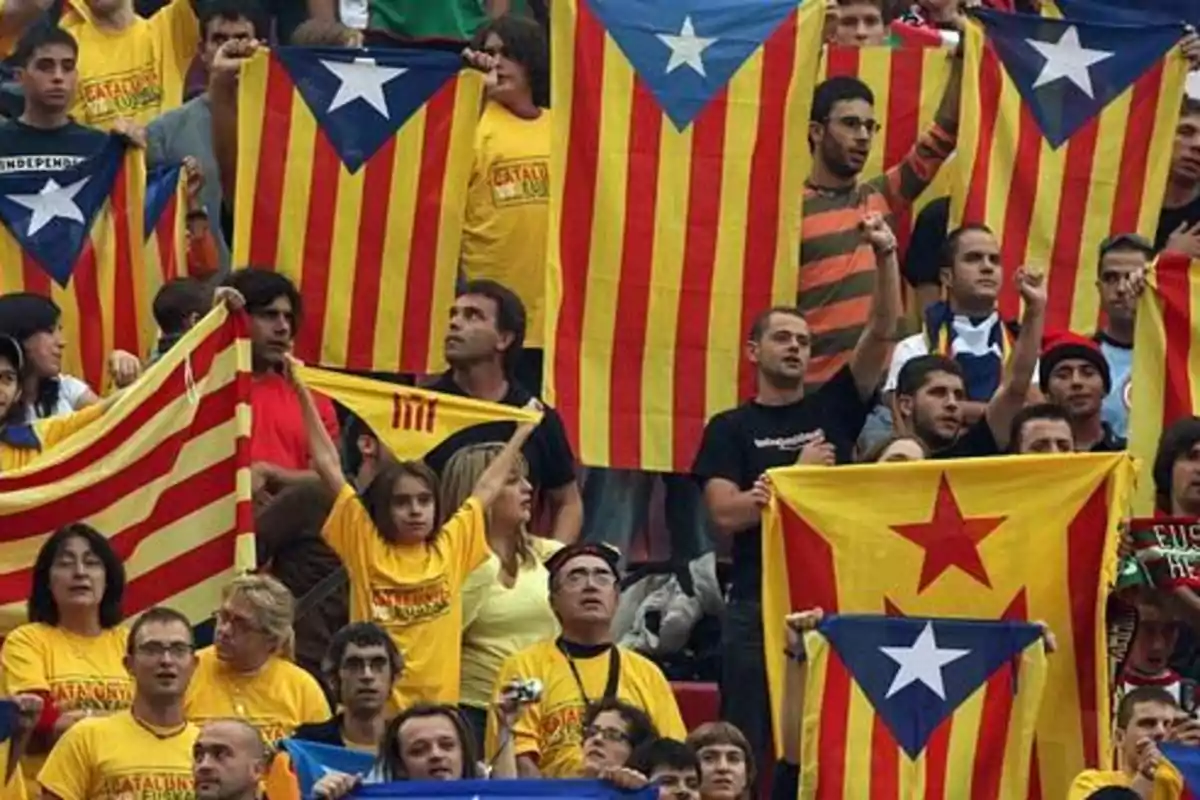 Personas reunidas sosteniendo banderas esteladas catalanas en un evento mostrando apoyo al independentismo de Cataluña Personas reunidas sosteniendo banderas esteladas catalanas en un evento mostrando apoyo al independentismo de Cataluña