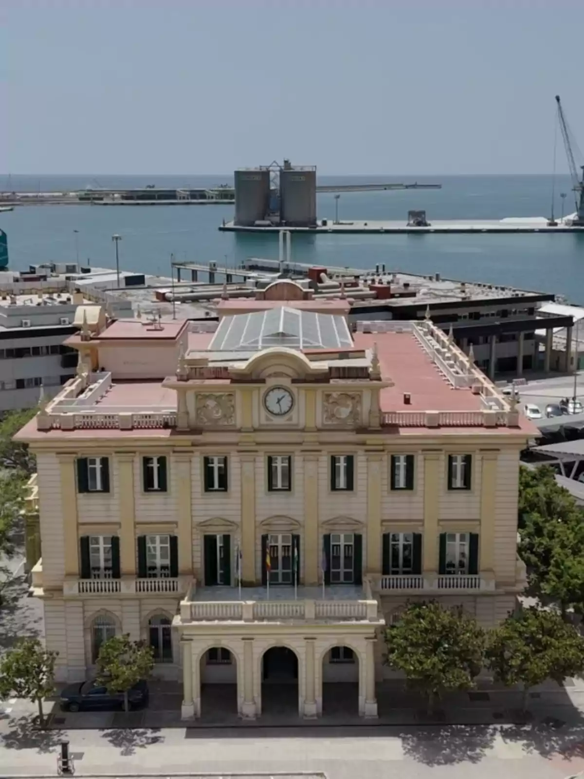 Edificio histórico de fachada amarilla con reloj en el centro y paneles solares en el techo frente a un puerto marítimo Edificio histórico de fachada amarilla con reloj en el centro y paneles solares en el techo frente a un puerto marítimo