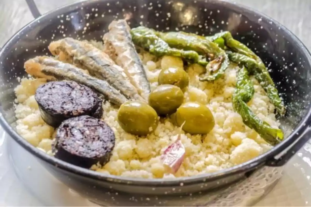 Plato tradicional con migas, aceitunas verdes, pimientos, sardinas y rodajas de morcilla servido en una sartén