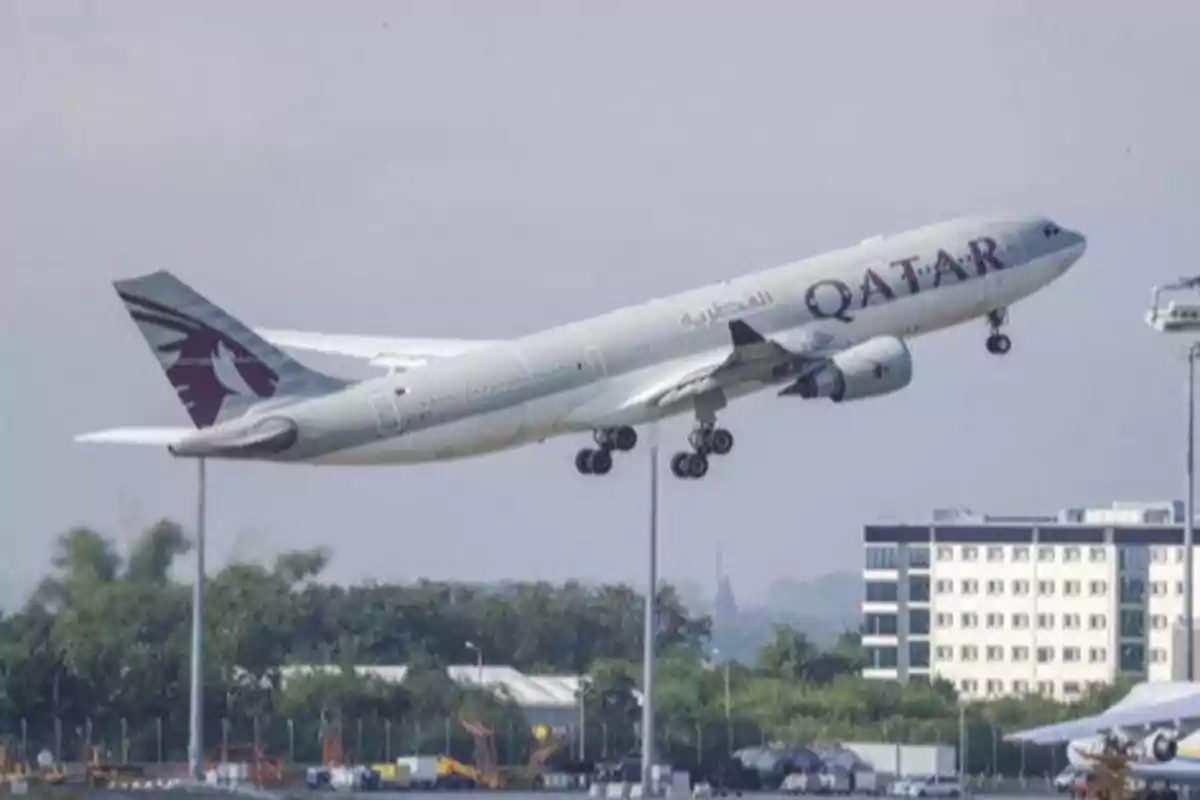 Avión de Qatar Airways despegando de un aeropuerto con edificios y vegetación al fondo Avión de Qatar Airways despegando de un aeropuerto con edificios y vegetación al fondo