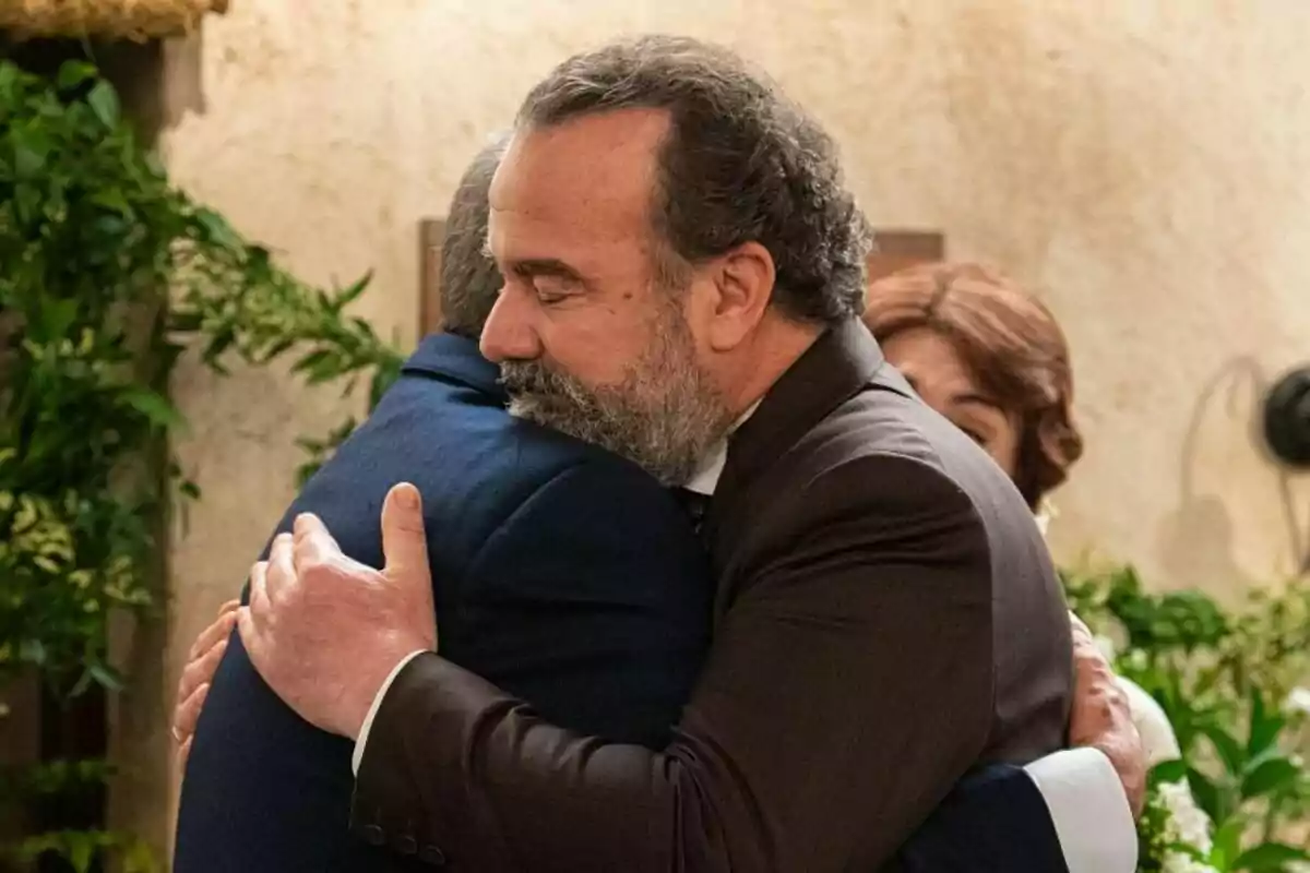 Dos hombres -uno de ellos Rómulo en 'La Promesa'- se abrazan con fuerza en un ambiente interior decorado con plantas, mostrando una expresión de consuelo y apoyo emocional. Dos hombres -uno de ellos Rómulo en 'La Promesa'- se abrazan con fuerza en un ambiente interior decorado con plantas, mostrando una expresión de consuelo y apoyo emocional.