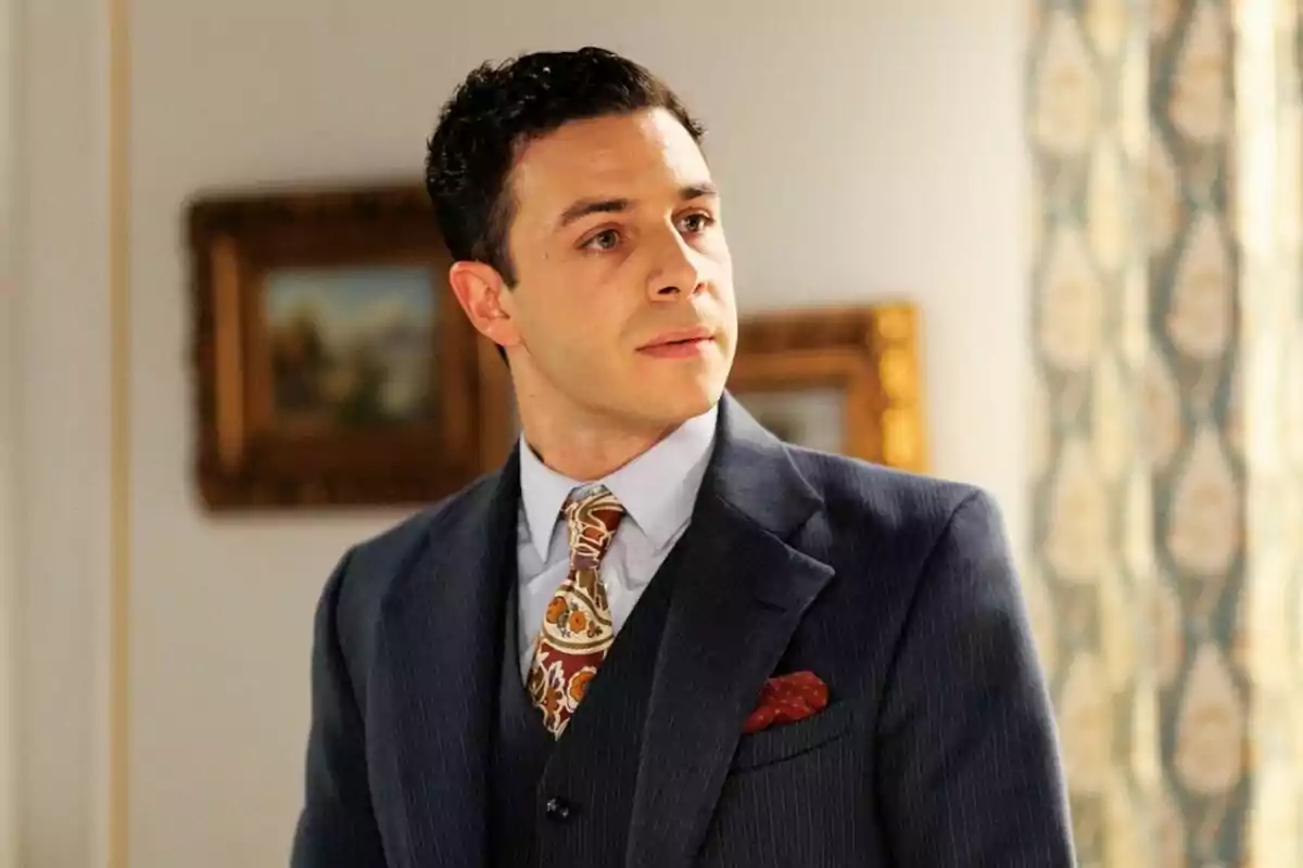 Pepe Nufrio vistiendo un traje azul y corbata estampada en una habitación elegante con cuadros y cortinas decorativas al fondo. Pepe Nufrio vistiendo un traje azul y corbata estampada en una habitación elegante con cuadros y cortinas decorativas al fondo.