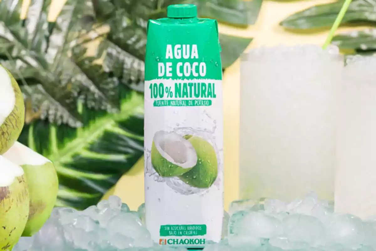 Envase de agua de coco 100% natural sobre una superficie con hielo rodeado de cocos y hojas verdes Envase de agua de coco 100% natural sobre una superficie con hielo rodeado de cocos y hojas verdes