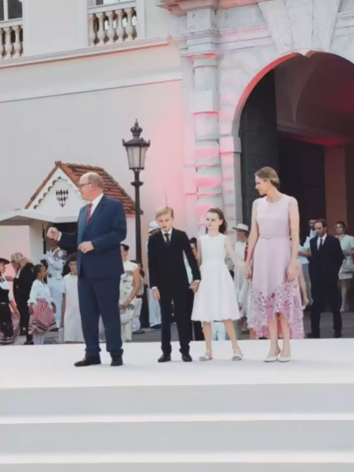 Cuatro personas elegantemente vestidas posan en una escalinata blanca frente a un edificio histórico mientras otras personas observan al fondo Cuatro personas elegantemente vestidas posan en una escalinata blanca frente a un edificio histórico mientras otras personas observan al fondo