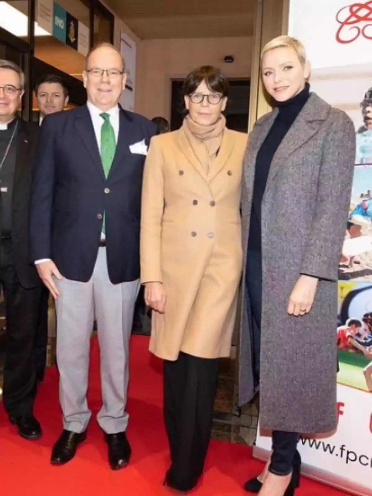 Three people pose on a red carpet at a formal event, two women and one man, all dressed elegantly and smiling at the camera. Three people pose on a red carpet at a formal event, two women and one man, all dressed elegantly and smiling at the camera.
