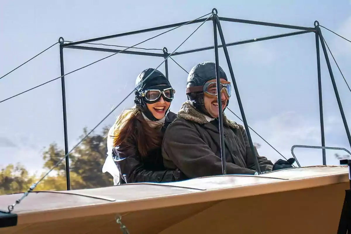 Arturo Sancho y Sara Font sonrientes con gafas y cascos de aviador disfrutan un paseo en un avión antiguo en La Promesa Arturo Sancho y Sara Font sonrientes con gafas y cascos de aviador disfrutan un paseo en un avión antiguo en La Promesa