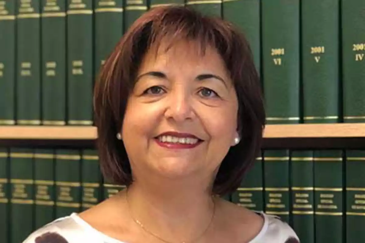 Mujer de cabello corto y oscuro sonriendo frente a una estantería con libros verdes Mujer de cabello corto y oscuro sonriendo frente a una estantería con libros verdes