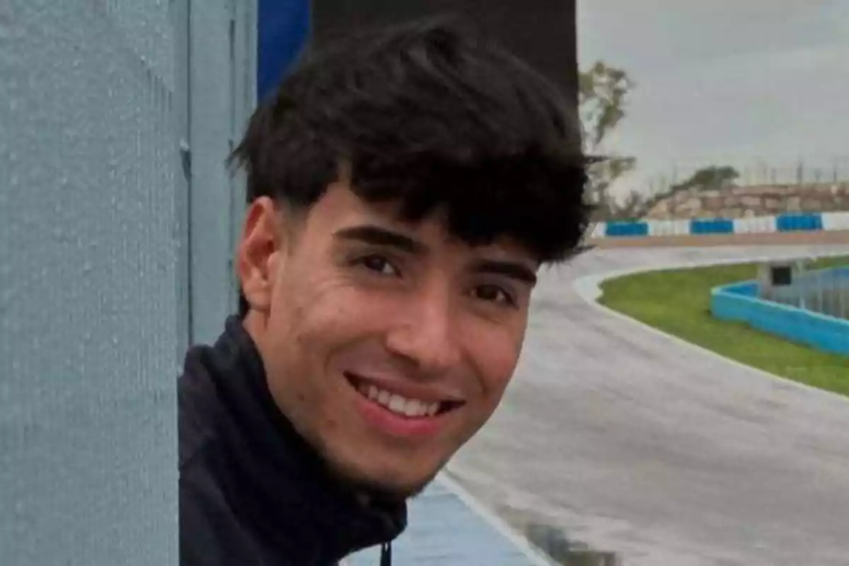 Joven sonriendo junto a una pista de carreras en un día nublado Joven sonriendo junto a una pista de carreras en un día nublado
