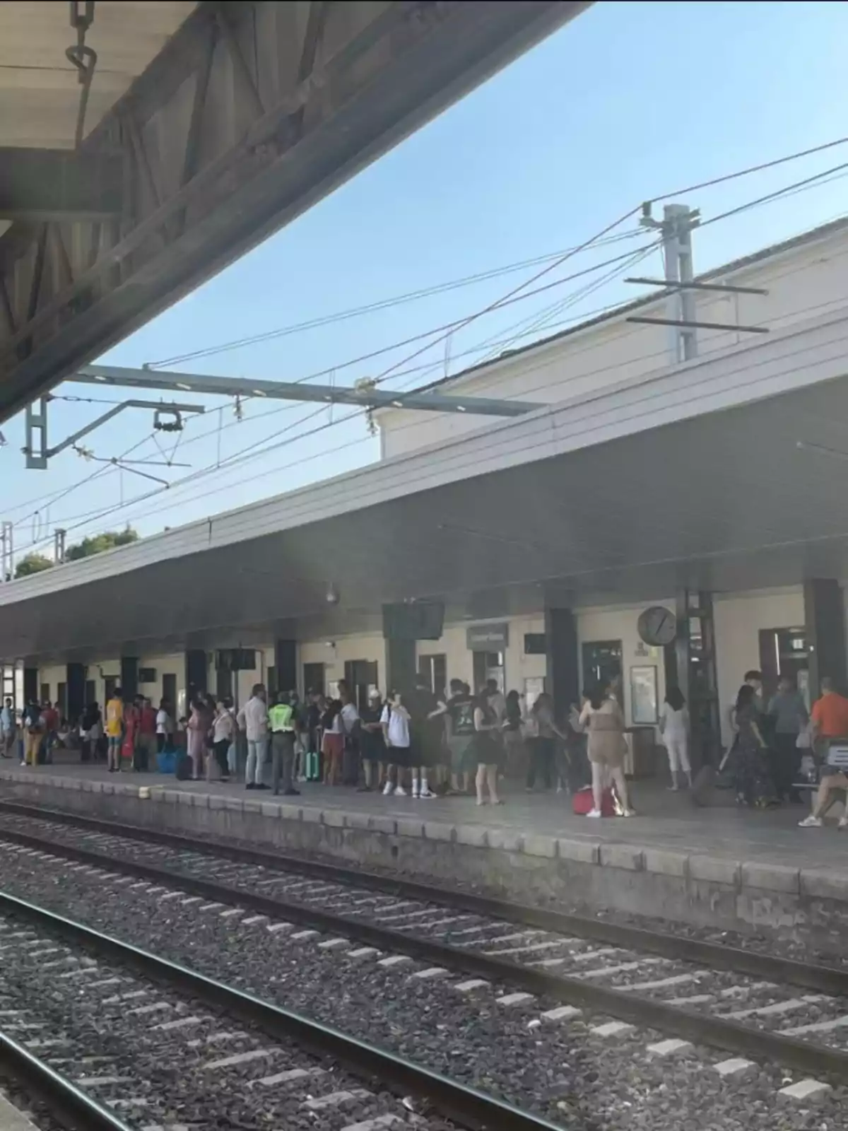 Personas esperando en el andén de una estación de tren bajo un cielo despejado Personas esperando en el andén de una estación de tren bajo un cielo despejado