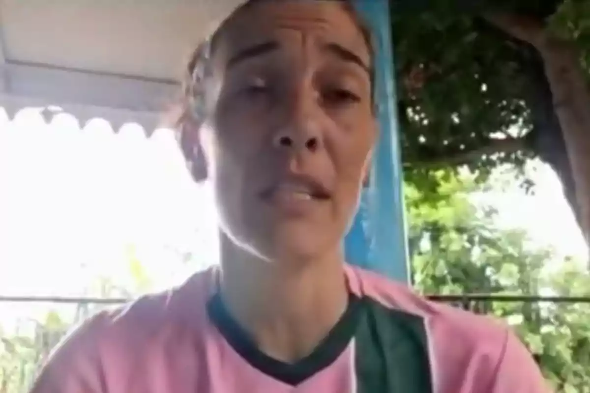 Mujer con camiseta rosa y verde hablando frente a la cámara en un entorno al aire libre con árboles al fondo Mujer con camiseta rosa y verde hablando frente a la cámara en un entorno al aire libre con árboles al fondo