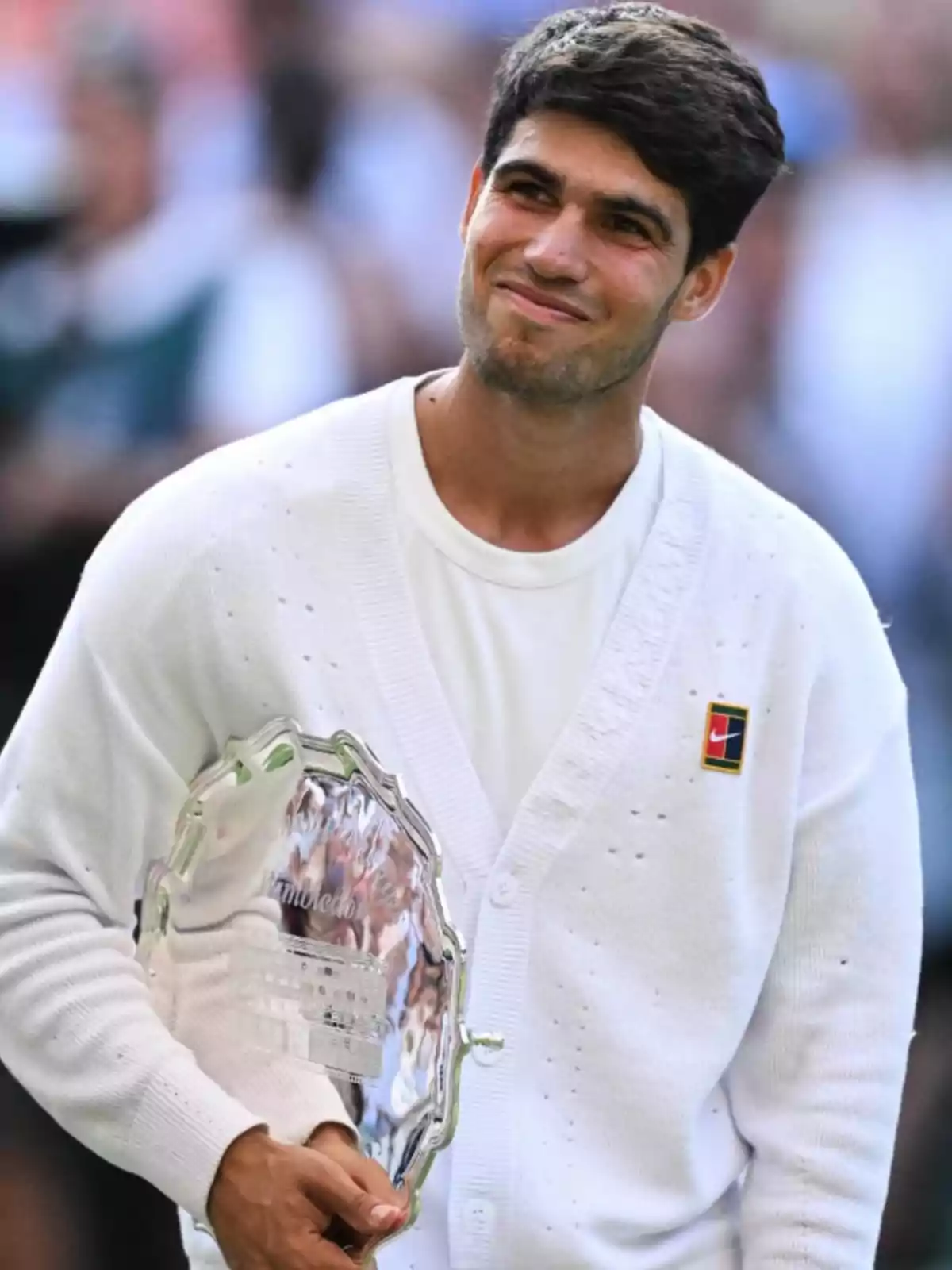 Joven tenista sonriente con suéter blanco sostiene un trofeo plateado en una ceremonia deportiva Joven tenista sonriente con suéter blanco sostiene un trofeo plateado en una ceremonia deportiva
