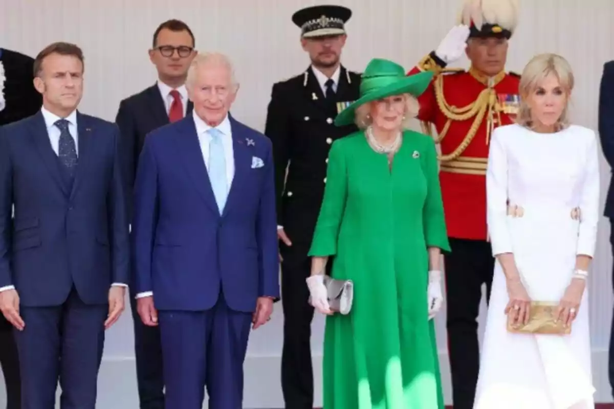Cuatro personas elegantemente vestidas posan para una foto oficial junto a miembros del personal de seguridad y un guardia con uniforme rojo Cuatro personas elegantemente vestidas posan para una foto oficial junto a miembros del personal de seguridad y un guardia con uniforme rojo