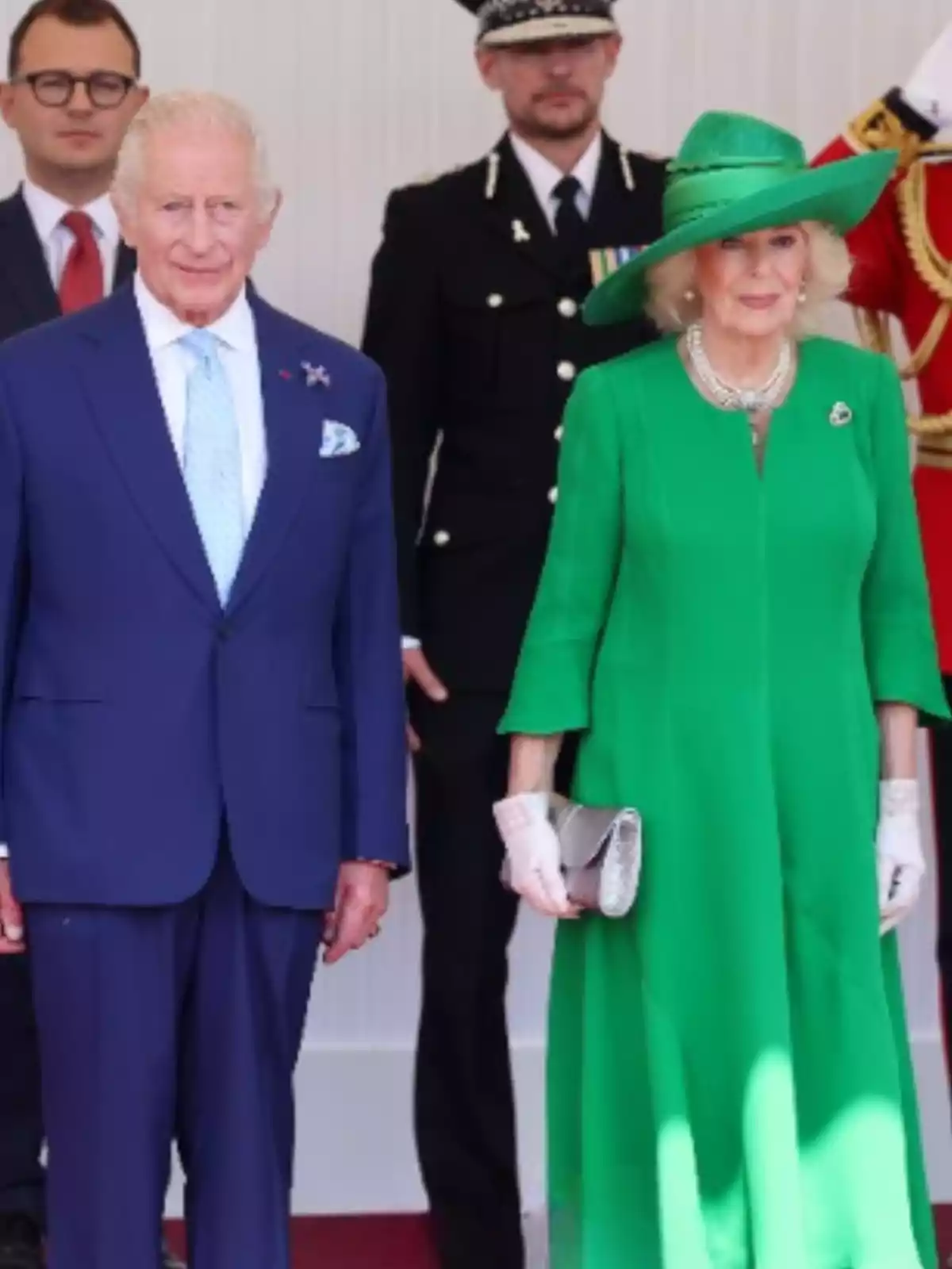 Pareja elegantemente vestida posando en un evento formal con personas uniformadas al fondo Pareja elegantemente vestida posando en un evento formal con personas uniformadas al fondo